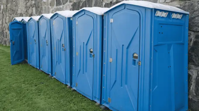 Row of blue portable toilets lined up on grass against a stone wall for event sanitation in Boulder, CO