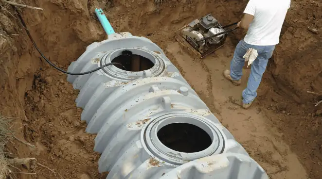 Septic tank installation showing a technician compacting soil around a new poly septic tank in an excavation pit in Boulder, CO
